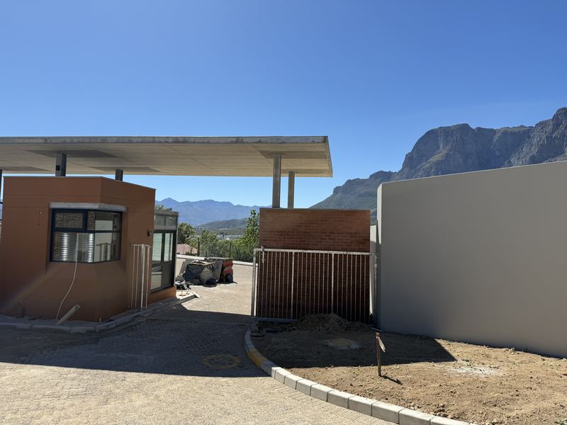 Gatehouse with a flat canopy roof, a gate and a boundary wall, with mountains behind