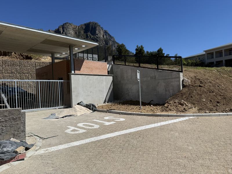 Paved entrance road with a STOP marking, the gatehouse canopy, a gate and concrete retaining walls